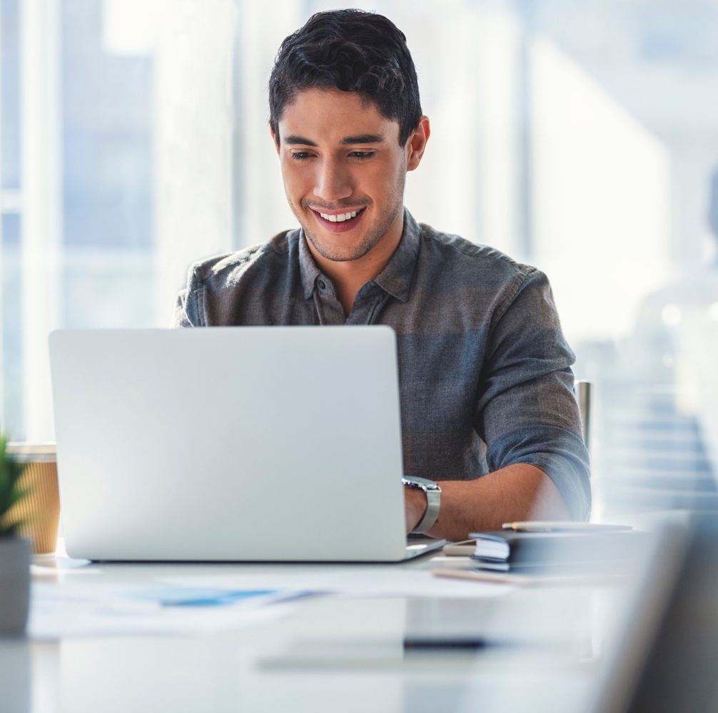 Smiling business owner sitting at a laptop, working on his trademark application